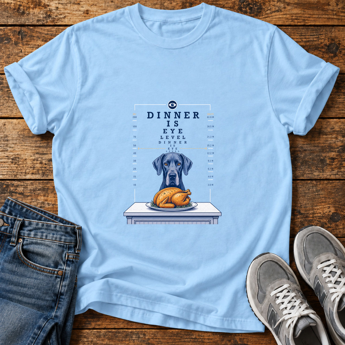 Dinner Eye Level Great Dane graphic T-shirt in Light Blue, shown on a flat-lay shirt mockup