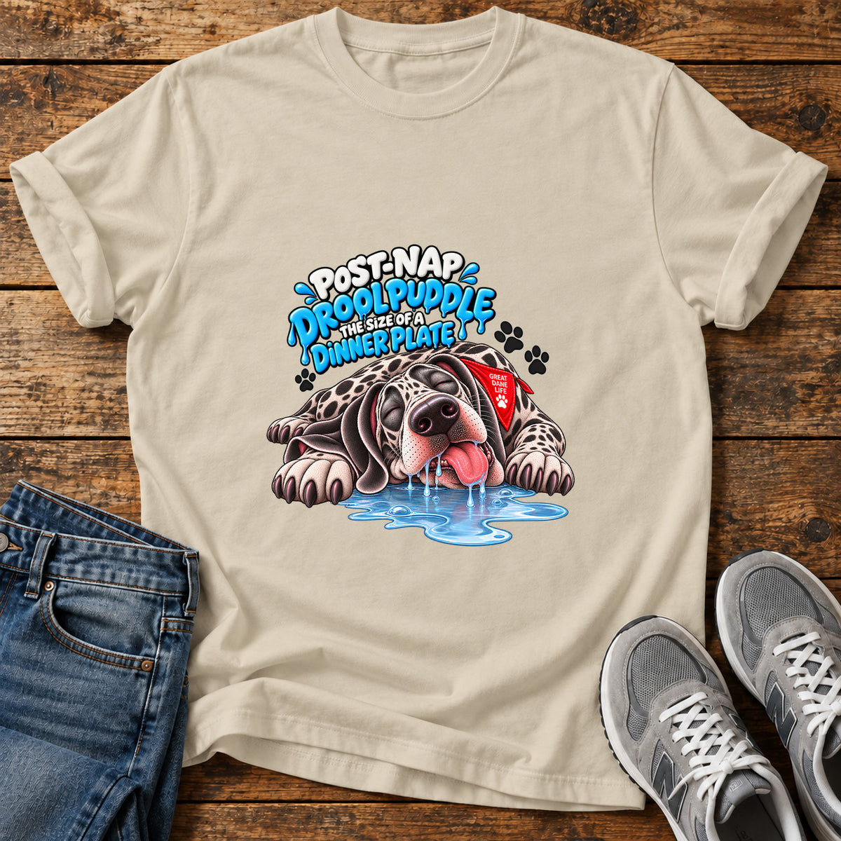 Drool Puddle Delight Great Dane graphic T-shirt in Sand, shown on a flat-lay shirt mockup