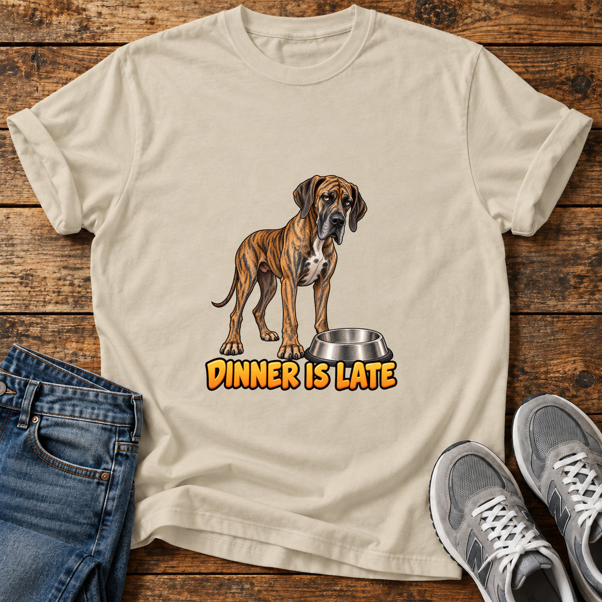 Dinner Is Late Great Dane graphic T-shirt in Sand, shown on a flat-lay shirt mockup
